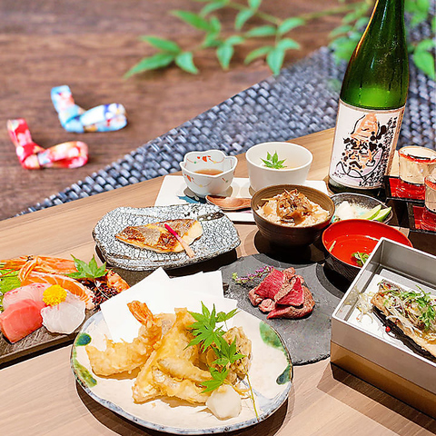 P048794660_480 ‣ 名古屋の飲食店企業/有限会社 坊’S Outdoor Japanese meal spread with sashimi, tempura, and small side dishes on a wooden table, bottle of sake in background