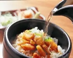 Hot stone pot of rice topped with chicken and vegetables as broth is poured into the dish.
